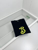 T-shirt nera con design giallo serpente in esposizione in negozio elegante e minimalista.