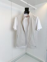Look elegante e minimalista con gilet grigio e t-shirt bianca su appendiabiti bianco.