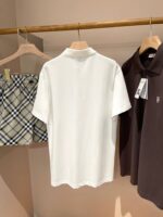 Esposizione minimalista di polo bianche, marroni e pantaloncini check beige su sfondo neutro.