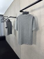 Vetrina minimalista con magliette grigie su rack moderni e sfondo in cemento chiaro.