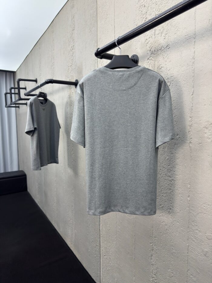Vetrina minimalista con magliette grigie su rack moderni e sfondo in cemento chiaro.