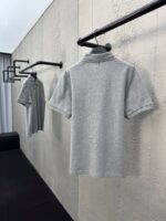 Magliette polo grige minimaliste su appendini neri in ambiente moderno ed elegante.