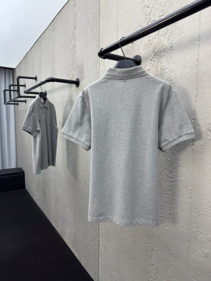 Magliette polo grige minimaliste su appendini neri in ambiente moderno ed elegante.