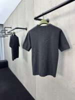 Magliette grigie minimaliste su rastrelliere nere, stile moderno e elegante, sfondo in parete testurizzata.