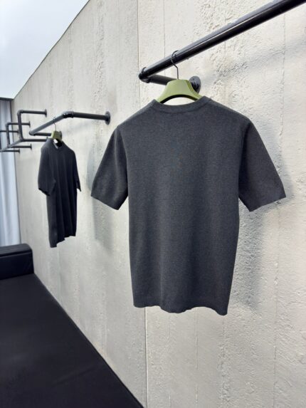 Magliette grigie minimaliste su rastrelliere nere, stile moderno e elegante, sfondo in parete testurizzata.