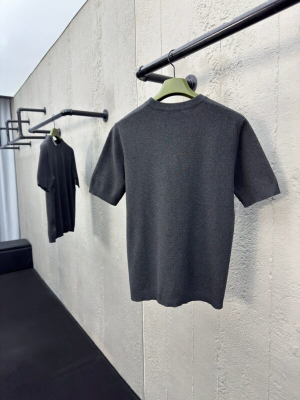Magliette grigie minimaliste su rastrelliere nere, stile moderno e elegante, sfondo in parete testurizzata.