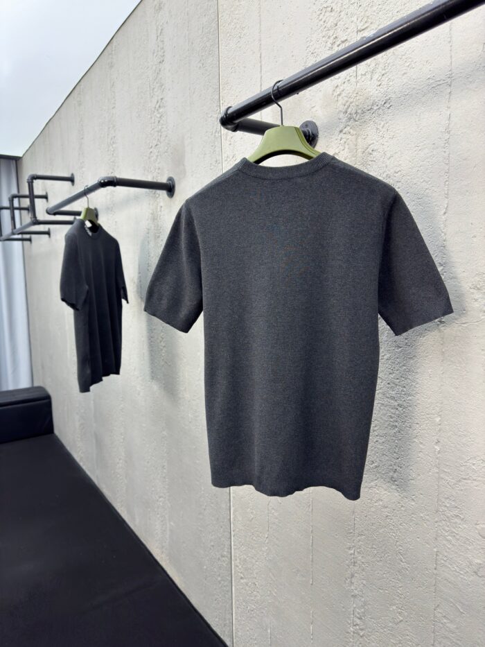 Magliette grigie minimaliste su rastrelliere nere, stile moderno e elegante, sfondo in parete testurizzata.