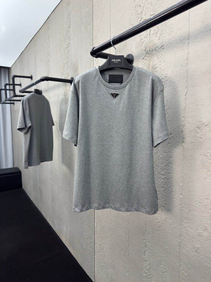 Maglietta grigia minimalista su esposizione moderna con parete ruvida, stile casual elegante.