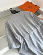 Maglietta grigia minimalista con borsa arancione, stile casual e moderno in ambiente semplice.