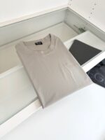Maglietta grigia minimalista su superficie bianca, ambientazione ordinata con accessorio scuro.