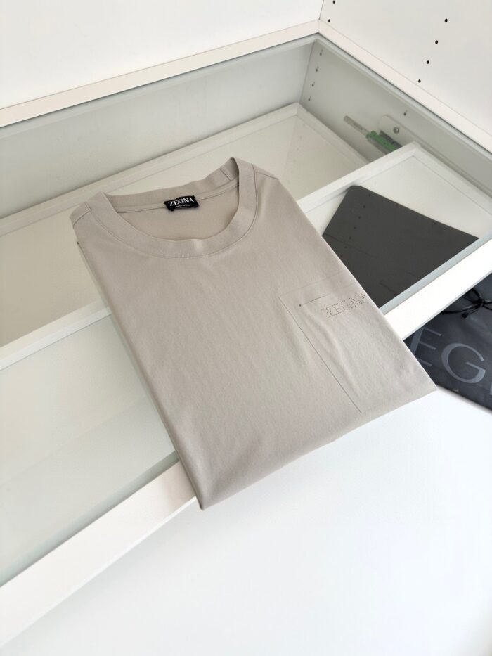 Maglietta grigia minimalista su superficie bianca, ambientazione ordinata con accessorio scuro.