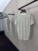 Magliette a righe bianche e navy su scaffali neri in ambiente moderno e minimalista.