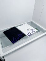 Esposizione di T-shirt di lusso in vetro minimalista, design elegante e contrasto bianco e nero.