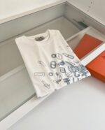 Maglietta bianca con disegni blu di oggetti creativi e packaging arancione elegante.