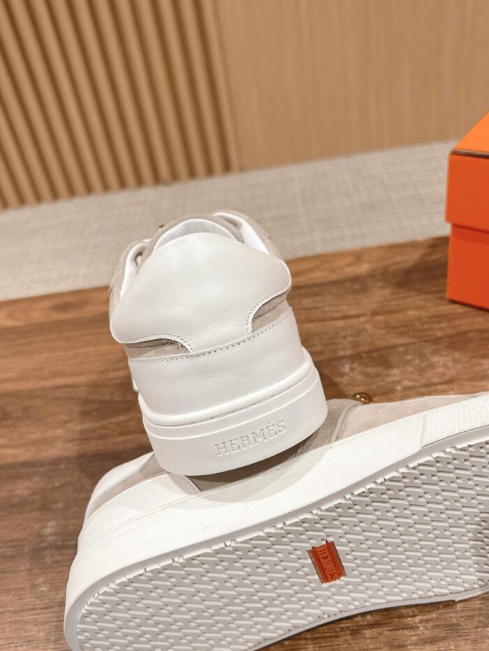 Sneakers bianche minimaliste su base di legno con scatola arancione, stile versatile ed elegante.
