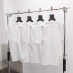 Esposizione elegante di quattro magliette bianche su rack moderno in negozio minimalista.