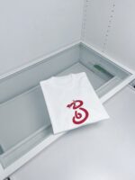 Maglietta bianca con grafica rossa, in vetrina espositiva moderna e minimalista.