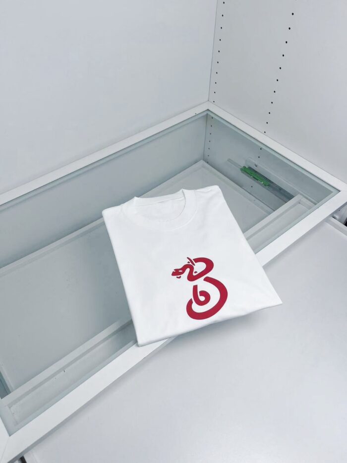 Maglietta bianca con grafica rossa, in vetrina espositiva moderna e minimalista.