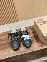 Sneakers New Balance nere con lacci mismatched su superficie di legno, stile casual ed elegante.