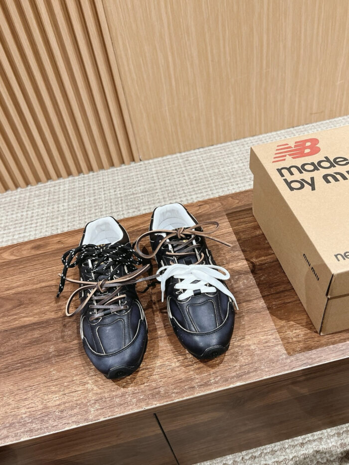 Sneakers New Balance nere con lacci mismatched su superficie di legno, stile casual ed elegante.