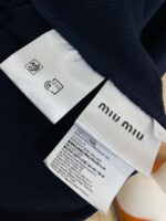 Etichetta Miu Miu con istruzioni di cura su tessuto navy, dettagli di marca e materiali