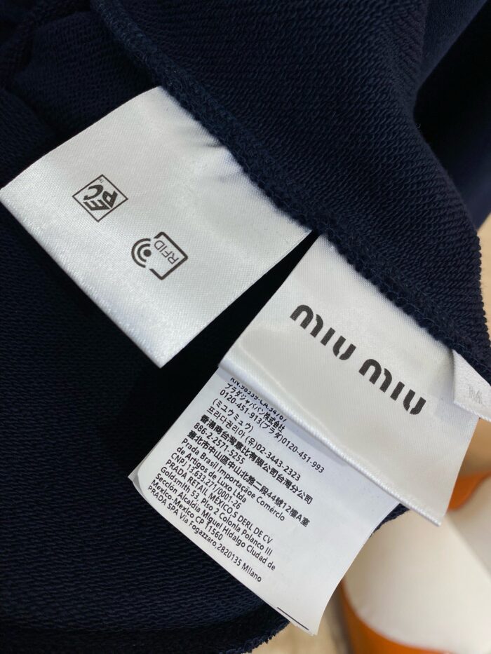 Etichetta Miu Miu con istruzioni di cura su tessuto navy, dettagli di marca e materiali