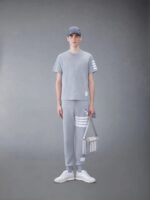 Modello maschile in outfit athleisure grigia con cappello, sneaker bianche e borsa strutturata.
