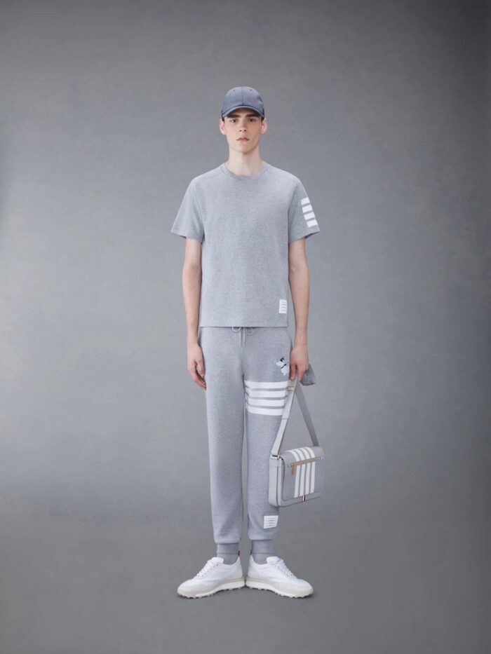 Modello maschile in outfit athleisure grigia con cappello, sneaker bianche e borsa strutturata.