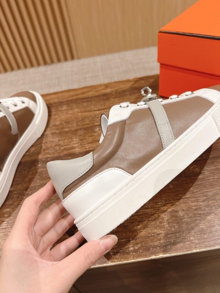 Sneaker beige e marrone moderna con dettagli eleganti su superficie di legno, scatola arancione.