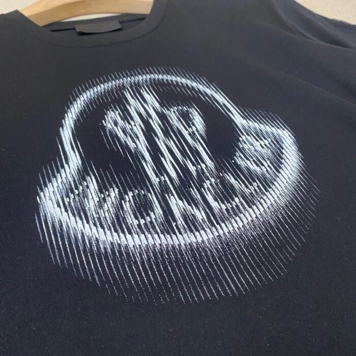 Maglietta nera con logo bianco astratto e moderno, stile urbano e di tendenza.