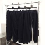 Pantaloni casual neri moderni con elastico, su stendino minimalista in ambiente luminoso.