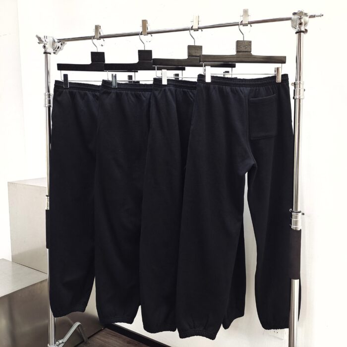 Pantaloni casual neri moderni con elastico, su stendino minimalista in ambiente luminoso.