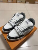 Sneakers di lusso bianche e grigie con cinturino, logo distintivo e design moderno.