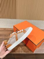 Sneaker casual moderna con tomaia beige e dettagli in pelle, accompagnata da scatola arancione vivace.