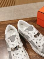 Sneakers moderne in pelle e tessuto con dettagli metallici, su tavolo di legno con scatola arancione.