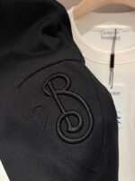 Giacca nera ricamata elegante e camicia crema casual su attaccapanni in legno.