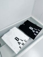 Esposizione elegante di T-Shirt bianca e nera con branding moderno su superficie in vetro trasparente.