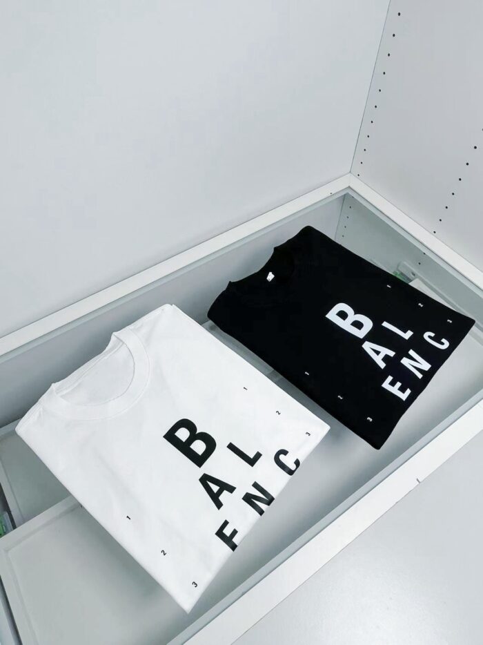 Esposizione elegante di T-Shirt bianca e nera con branding moderno su superficie in vetro trasparente.