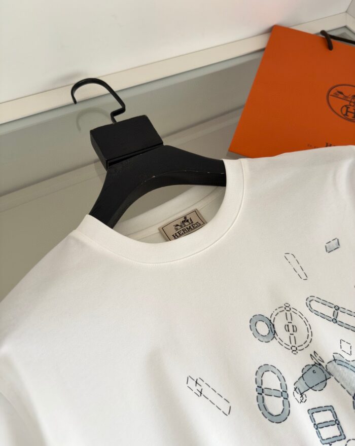 Maglietta bianca moderna con grafica geometrica, presentata su un appendino nel contesto di moda elegante.