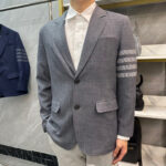 Uomo elegante con blazer grigio, camicia bianca e pantaloni chiari in stile moderno.