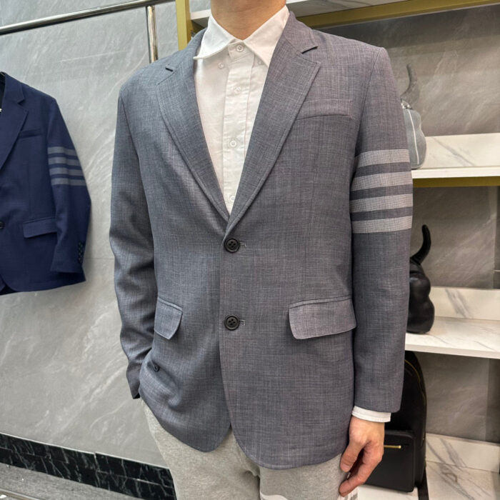 Uomo elegante con blazer grigio, camicia bianca e pantaloni chiari in stile moderno.