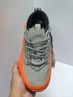 Scarpa sportiva grigia con dettagli arancioni, comfort, stile trendy e suola ammortizzata.