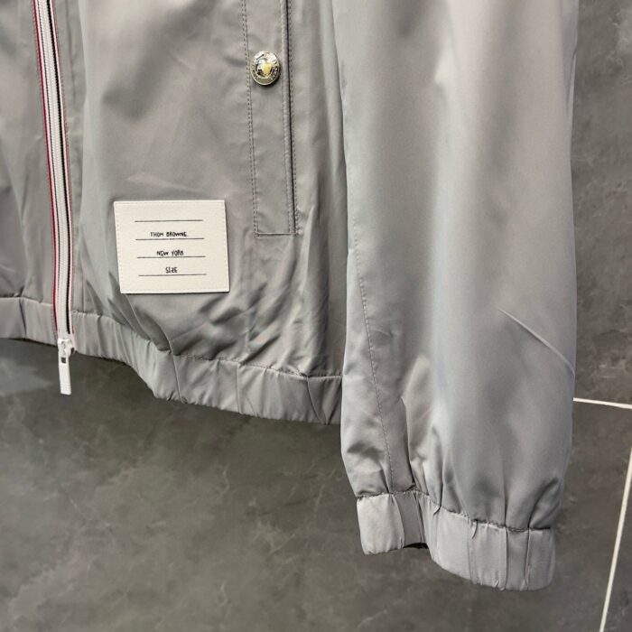 Giacca grigia moderna con bottoni a pressione, elastico ai polsini e design minimale.