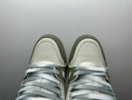 Sneakers verde e bianco in pelle con laccetti argentati e stile moderno su sfondo minimalista.