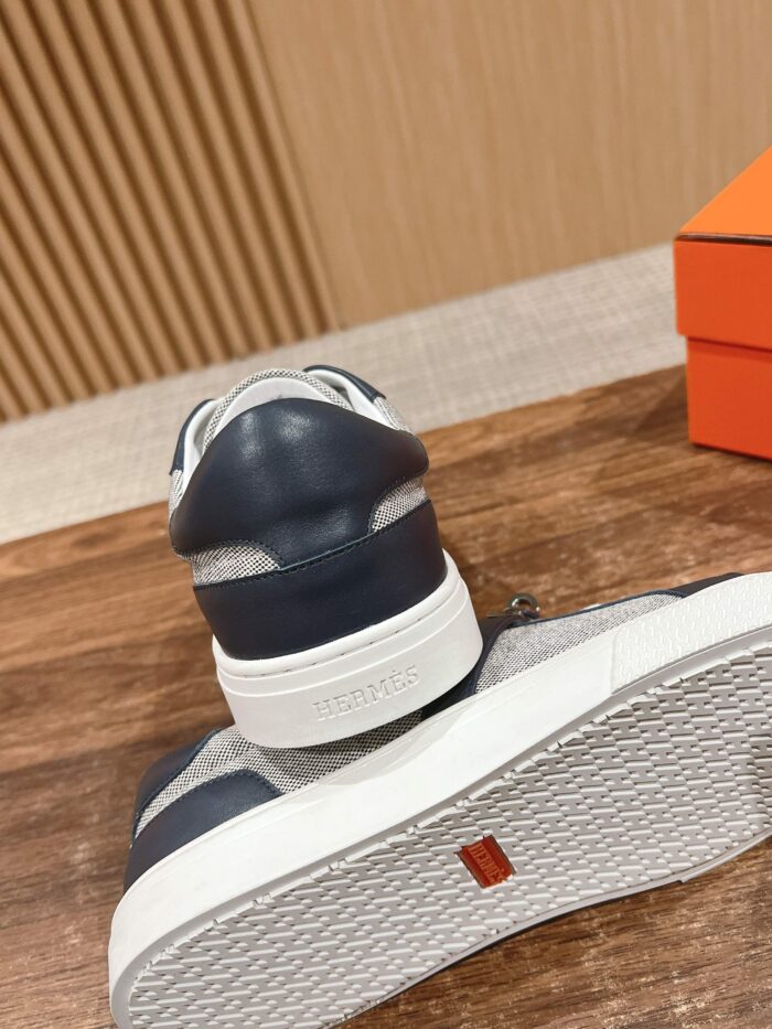 Sneakers grigi e navy su superficie in legno, con suola in gomma bianca e dettagli eleganti.