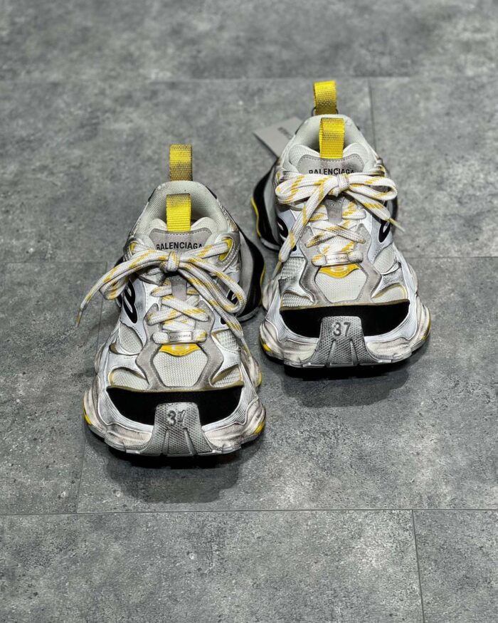 Sneakers grigie con dettagli gialli, design futuristico, suola chunky e materiali traspiranti.