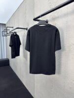 Magliette nere minimaliste su parete di cemento, stile urbano e moderno con luce naturale.
