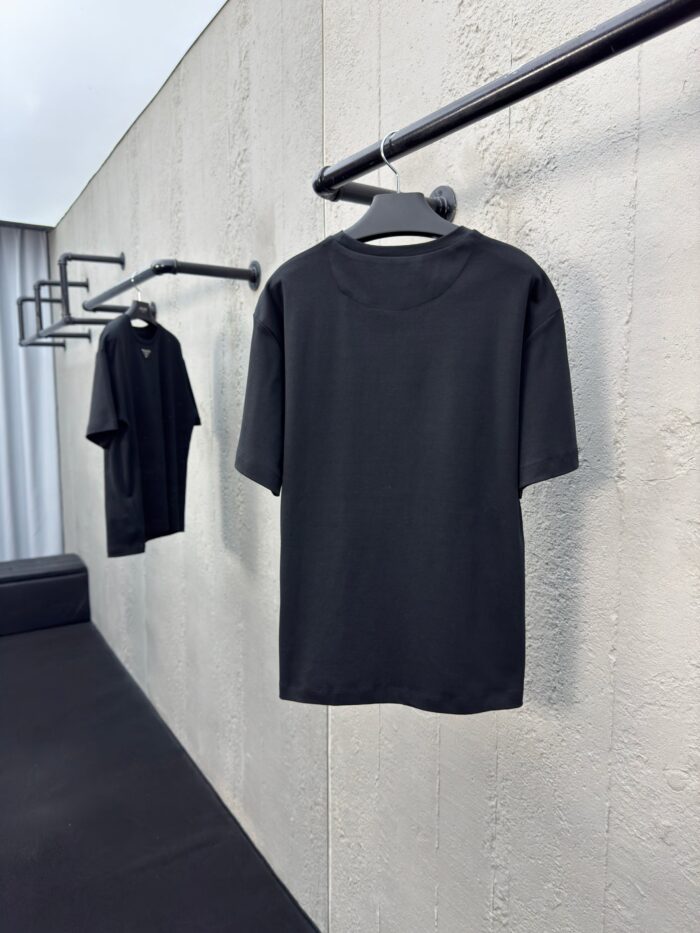 Magliette nere minimaliste su parete di cemento, stile urbano e moderno con luce naturale.