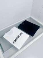 T-shirt bianca con logo Margiela e nera minimal in vetrina di moda esclusiva.
