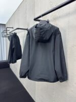 Giaccone grigio minimalista su appendiabiti nero in ambiente moderno e luminoso.